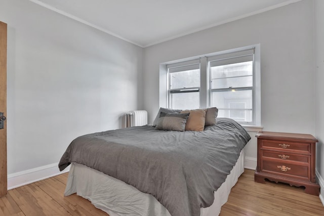 bedroom featuring radiator heating unit, light wood-style floors, baseboards, and ornamental molding