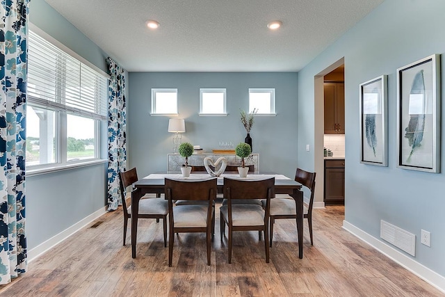 dining area with a textured ceiling and light hardwood / wood-style floors