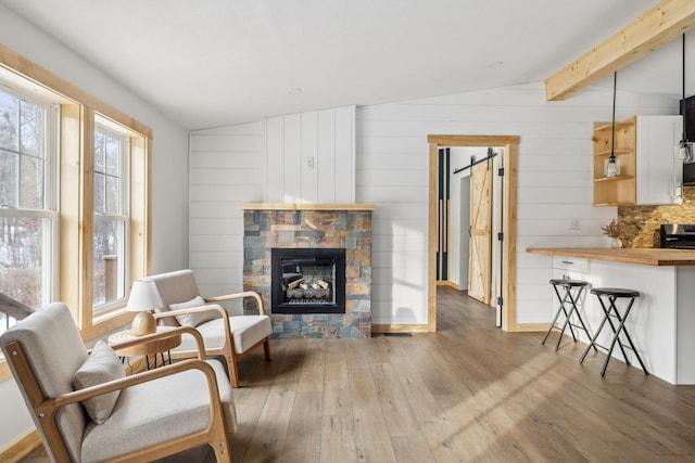 living room with wooden walls, a fireplace, light hardwood / wood-style flooring, and vaulted ceiling with beams