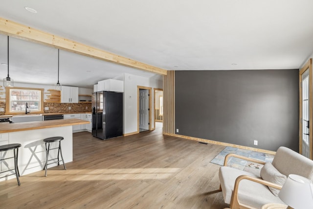 interior space with beamed ceiling, black appliances, a kitchen breakfast bar, pendant lighting, and white cabinets