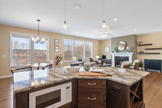 kitchen with a fireplace, a kitchen island, light stone counters, and decorative light fixtures