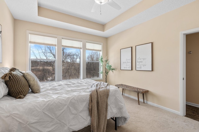 bedroom with ceiling fan, a tray ceiling, carpet flooring, and a textured ceiling