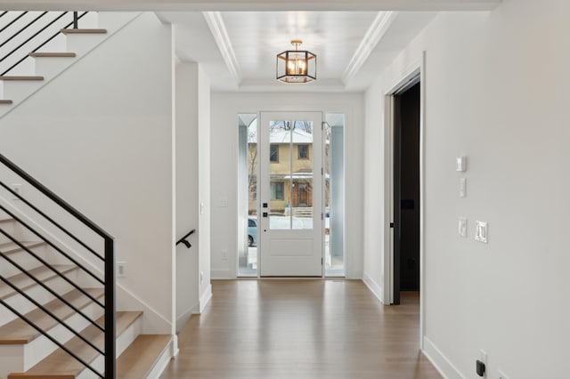 foyer with a tray ceiling, crown molding, a chandelier, and hardwood / wood-style flooring