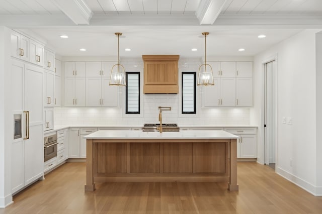 kitchen featuring hanging light fixtures, white cabinetry, beamed ceiling, and a kitchen island with sink