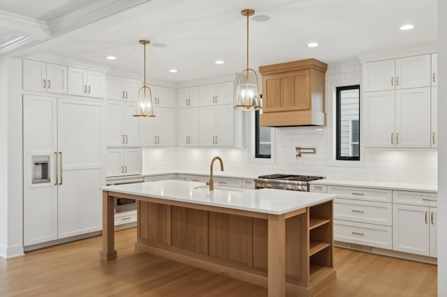 kitchen with hanging light fixtures, white cabinets, sink, and a center island with sink