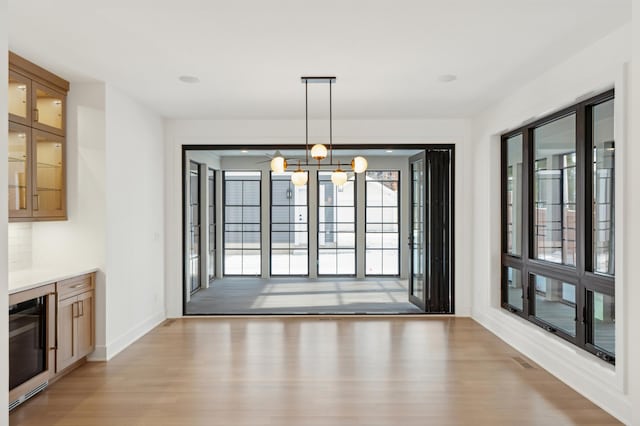 unfurnished dining area featuring wine cooler, an inviting chandelier, and light hardwood / wood-style flooring