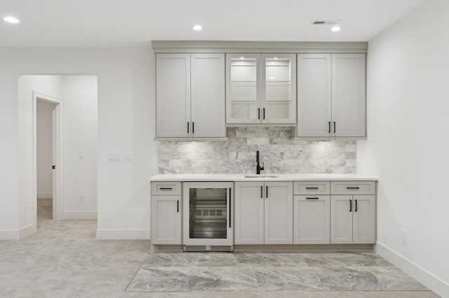 bar with light colored carpet, sink, gray cabinets, tasteful backsplash, and beverage cooler