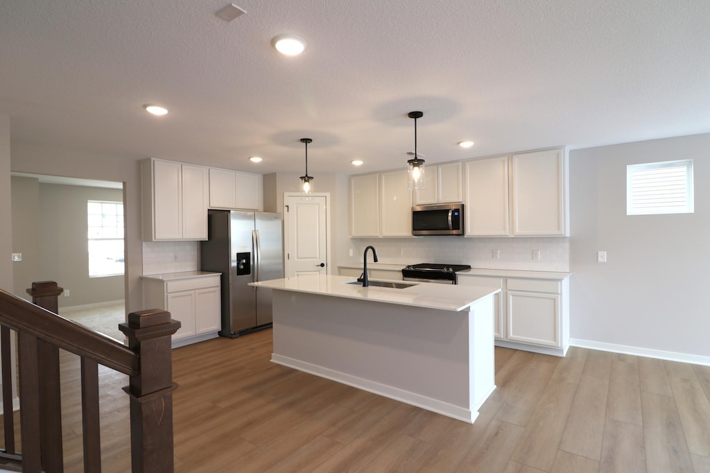 kitchen featuring sink, appliances with stainless steel finishes, hanging light fixtures, an island with sink, and white cabinets