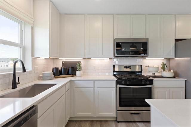 kitchen with stainless steel appliances, tasteful backsplash, light countertops, light wood-style flooring, and a sink