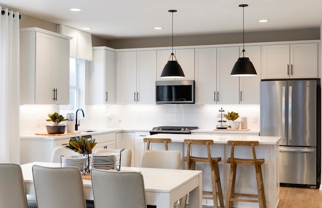 kitchen with white cabinetry, hanging light fixtures, a kitchen island, and appliances with stainless steel finishes