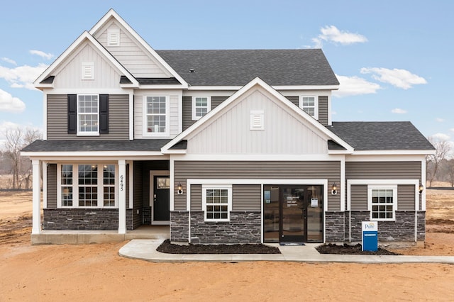 view of front facade with roof with shingles, board and batten siding, and stone siding