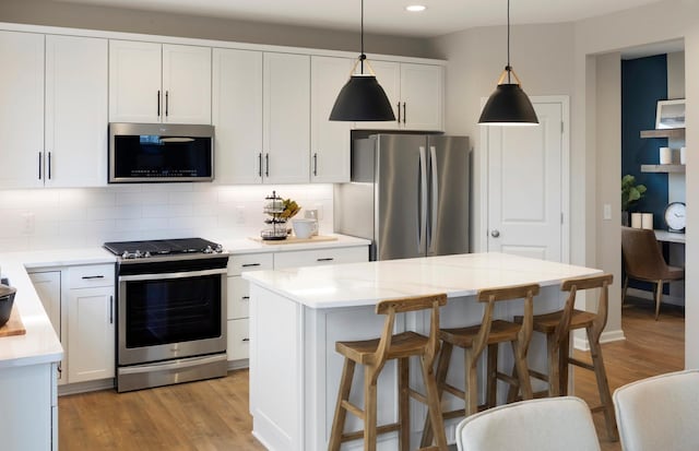 kitchen with hanging light fixtures, decorative backsplash, appliances with stainless steel finishes, light wood-style floors, and white cabinets