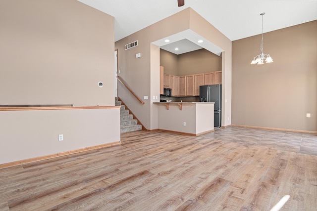 unfurnished living room with a high ceiling, a chandelier, and light hardwood / wood-style flooring