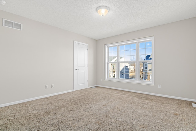 empty room with carpet, a textured ceiling, visible vents, and baseboards