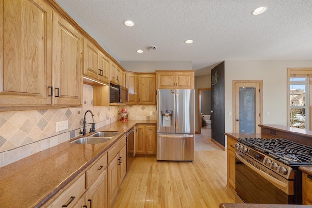 kitchen with light wood finished floors, tasteful backsplash, appliances with stainless steel finishes, a sink, and dark stone counters