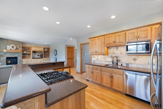 kitchen with light wood-style flooring, stainless steel appliances, a fireplace, a sink, and open floor plan