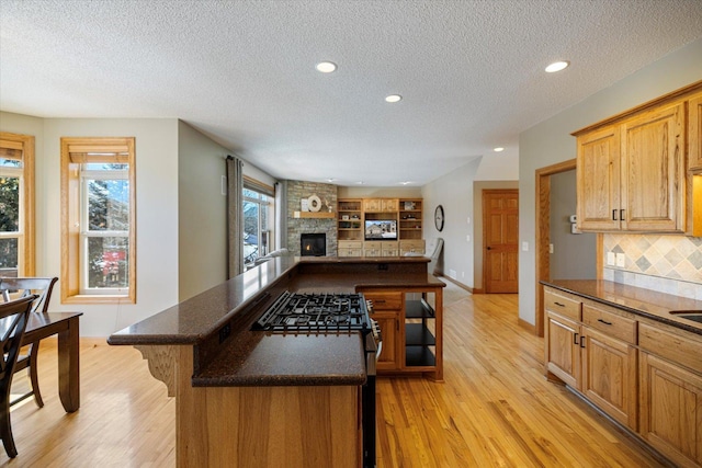 kitchen with light wood-style flooring, a center island, open floor plan, and a stone fireplace