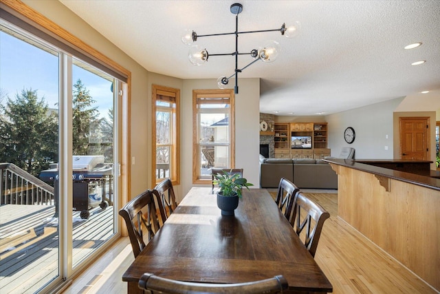 dining area with a large fireplace, light wood finished floors, a textured ceiling, and an inviting chandelier