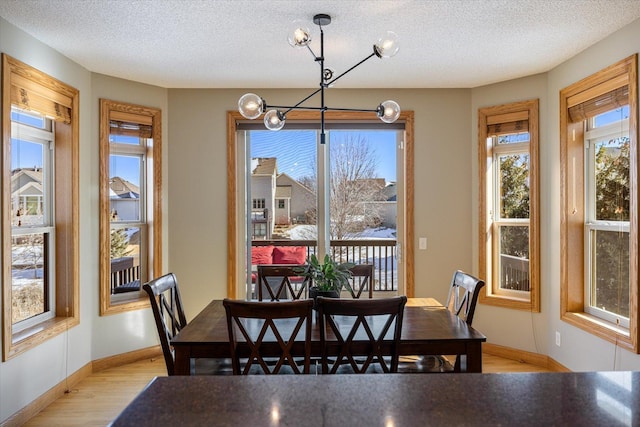 dining space featuring baseboards, light wood-style flooring, and a textured ceiling