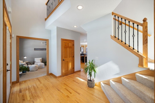 foyer entrance featuring light wood-type flooring, a towering ceiling, recessed lighting, and stairs