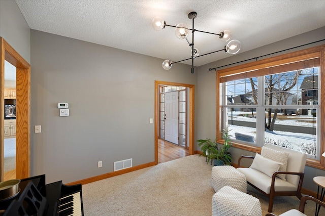 living area featuring visible vents, light carpet, baseboards, and a textured ceiling