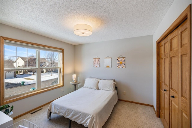 bedroom with light carpet, baseboards, visible vents, a textured ceiling, and a closet