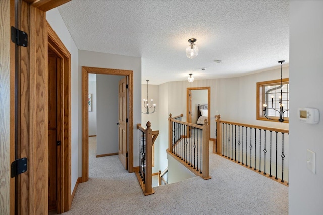 hall with carpet, a notable chandelier, a textured ceiling, an upstairs landing, and baseboards