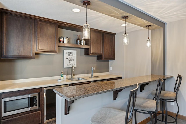 kitchen featuring dark brown cabinets, stainless steel microwave, a sink, and a kitchen breakfast bar