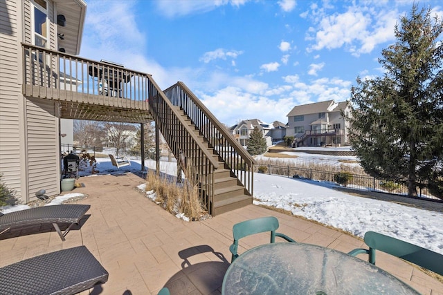 snow covered patio with a residential view, outdoor dining area, fence, and stairway