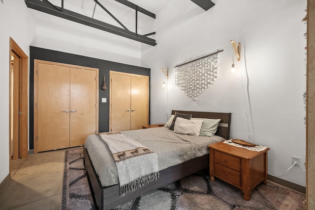 bedroom featuring multiple closets, a towering ceiling, and concrete floors