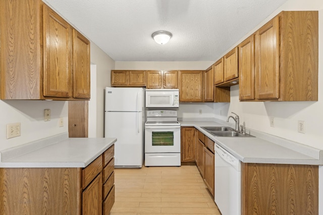 kitchen with white appliances, sink, a textured ceiling, and light wood-type flooring