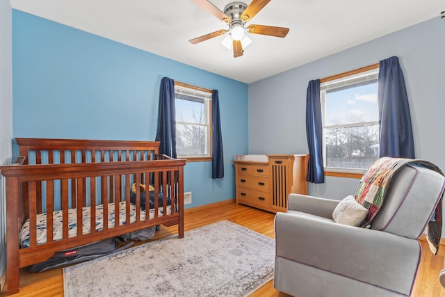 bedroom with ceiling fan, a nursery area, and light wood-type flooring