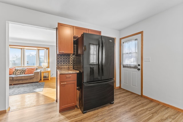 kitchen featuring light hardwood / wood-style flooring, backsplash, light stone counters, and black fridge