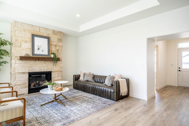 living room with a stone fireplace, light wood-type flooring, and a tray ceiling