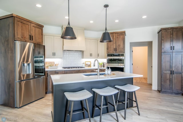 kitchen featuring an island with sink, appliances with stainless steel finishes, sink, and light hardwood / wood-style flooring