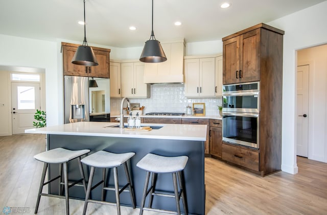 kitchen featuring stainless steel appliances, an island with sink, white cabinets, and light hardwood / wood-style floors