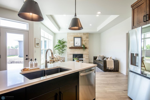 kitchen featuring sink, hanging light fixtures, stainless steel appliances, light hardwood / wood-style floors, and a raised ceiling