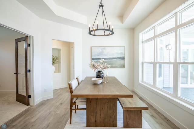 dining room featuring a raised ceiling, a notable chandelier, french doors, and light hardwood / wood-style flooring