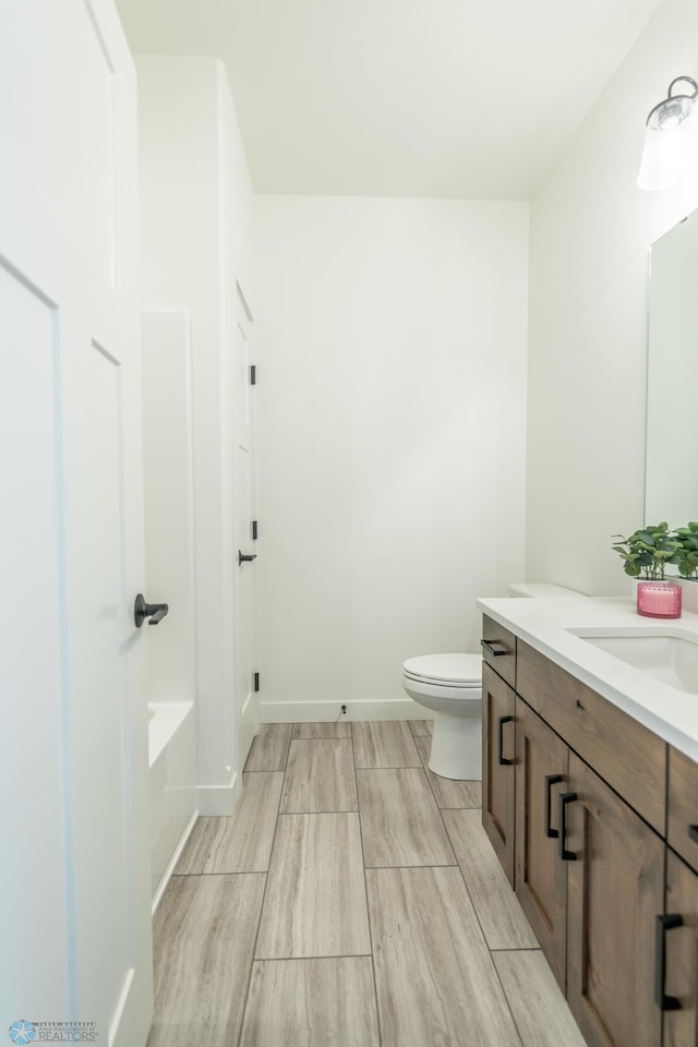 full bath featuring toilet, a washtub, vanity, and baseboards