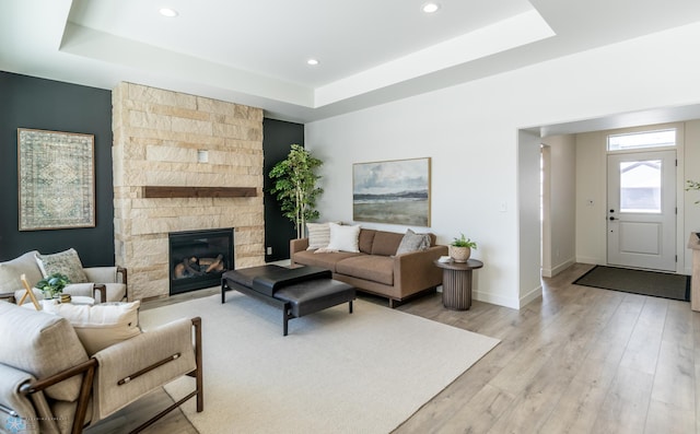 living room featuring recessed lighting, a fireplace, baseboards, light wood finished floors, and a raised ceiling