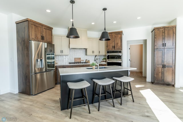 kitchen with stainless steel appliances, a sink, a kitchen breakfast bar, decorative backsplash, and decorative light fixtures