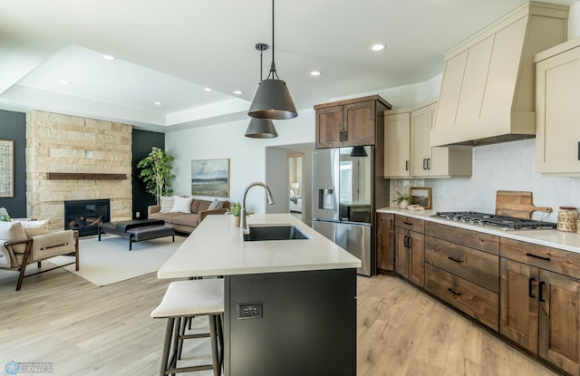 kitchen with stainless steel appliances, a fireplace, a sink, light countertops, and custom range hood