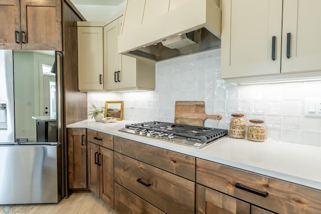 kitchen featuring stainless steel appliances, light countertops, backsplash, and extractor fan