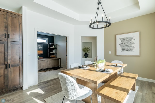 dining space featuring a notable chandelier, a tray ceiling, baseboards, and light wood-style floors