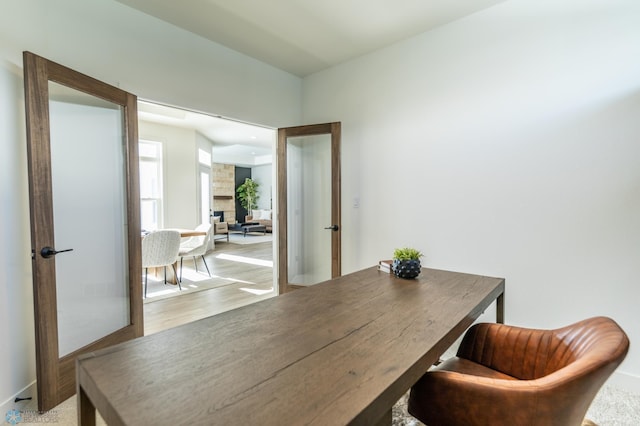 office area with light wood-type flooring, french doors, and a stone fireplace