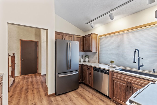 kitchen featuring lofted ceiling, sink, light stone counters, light hardwood / wood-style flooring, and appliances with stainless steel finishes