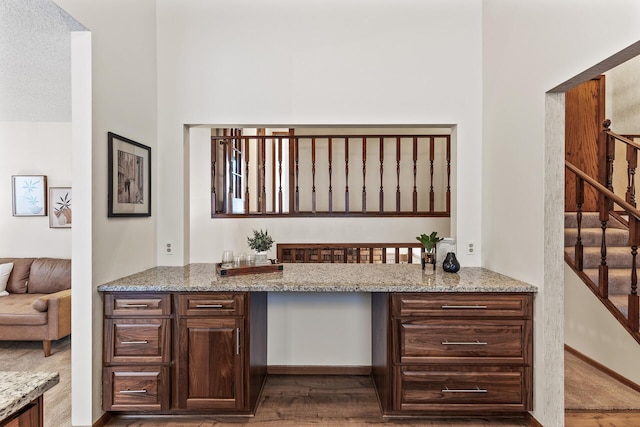 bar featuring dark brown cabinetry, wood-type flooring, and light stone counters