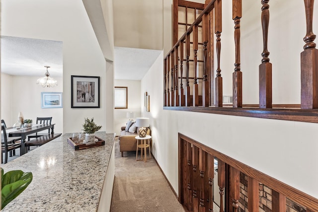 hallway with light colored carpet, a notable chandelier, and a textured ceiling