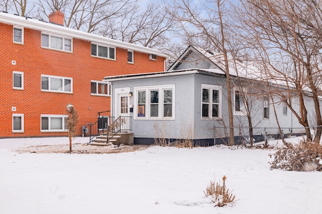 snow covered house featuring brick siding, a chimney, and fence