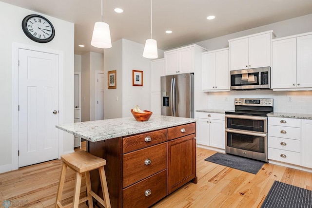 kitchen with pendant lighting, appliances with stainless steel finishes, a kitchen island, tasteful backsplash, and light stone counters